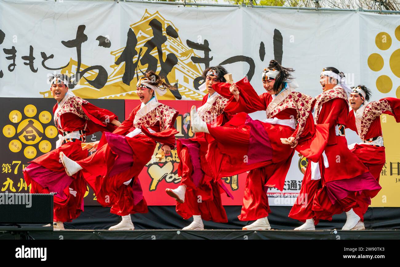 Squadra di ballerini giapponesi yosakoi sul palco che balla con gonne rosse e tuniche yukata a maniche lunghe tenendo naruko e clappers. Kyusyu Gassai festival. Foto Stock
