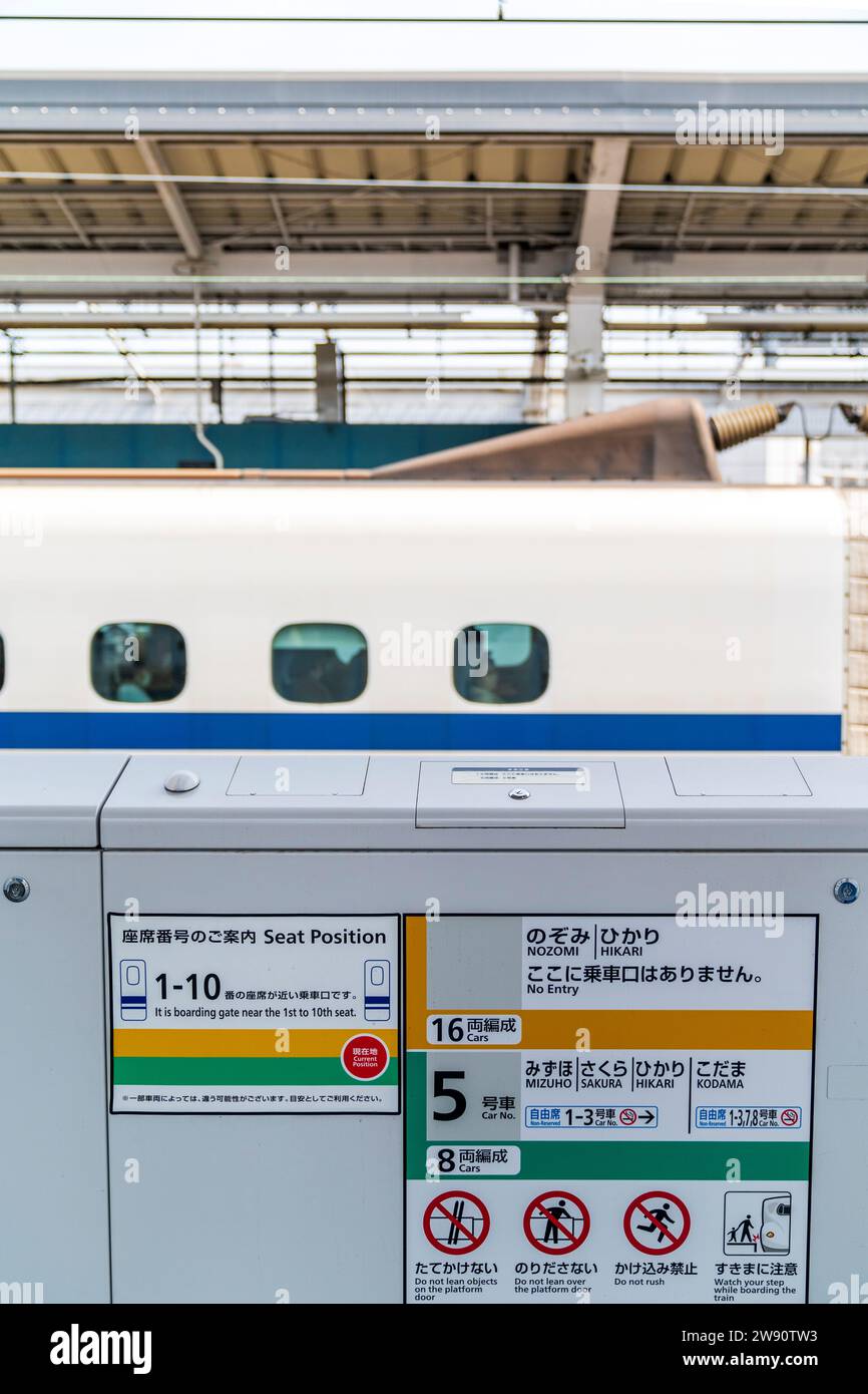 Cancello d'imbarco con posti a sedere e numeri mostrati per i vari tipi di shinkansen, treno ad alta velocità, sul binario di Okayama. Allenati dietro. Foto Stock