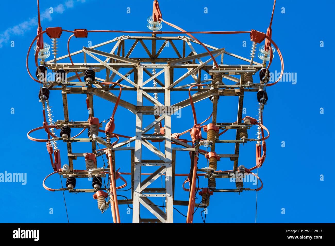 Cima di una torre di linea elettrica con cavi e dettagli rossi, vista da sotto, con cielo blu. Immagine orizzontale Foto Stock
