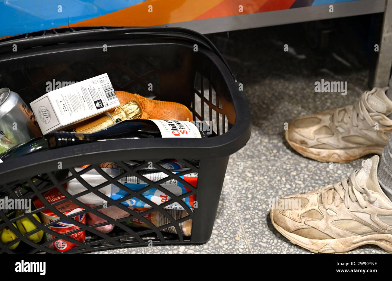 Cestino con cibo al piano del supermercato accanto ai piedi dei clienti Foto Stock