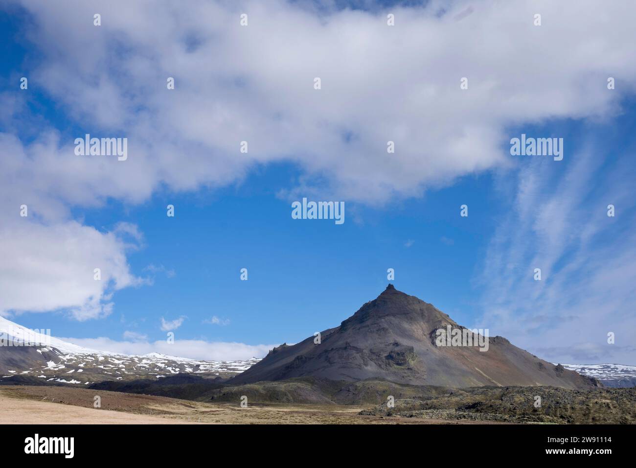Ripida montagna in Islanda con un bel cielo blu, nuvole e sole. Montagne innevate sullo sfondo Foto Stock