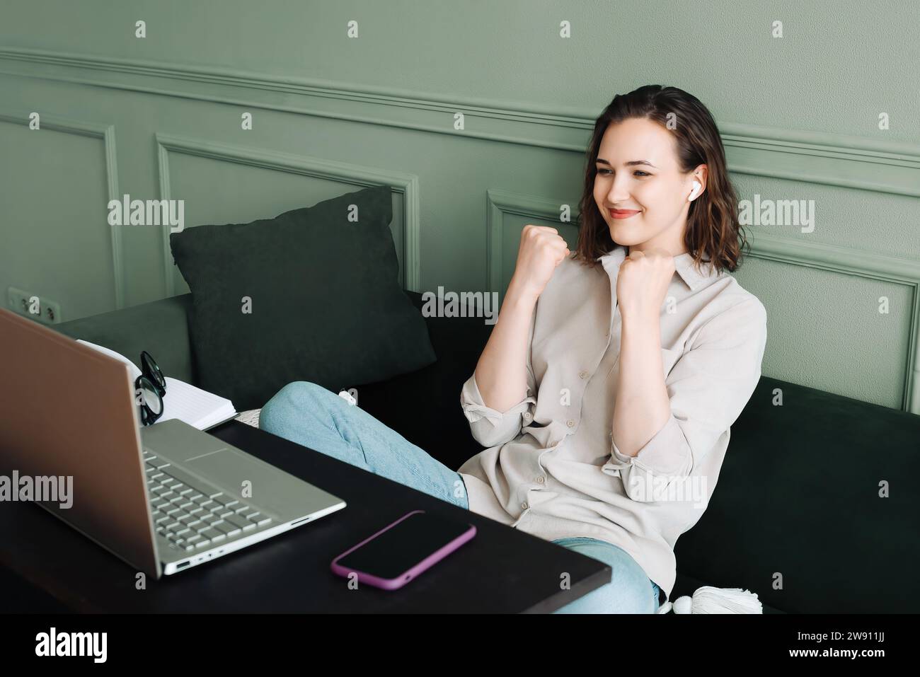 Vincere e festeggiare. Donna sorridente che si muove in una video chat di successo sul suo laptop. La donna felice con gli occhiali sta trasmettendo via radio mentre comunica su di lui Foto Stock