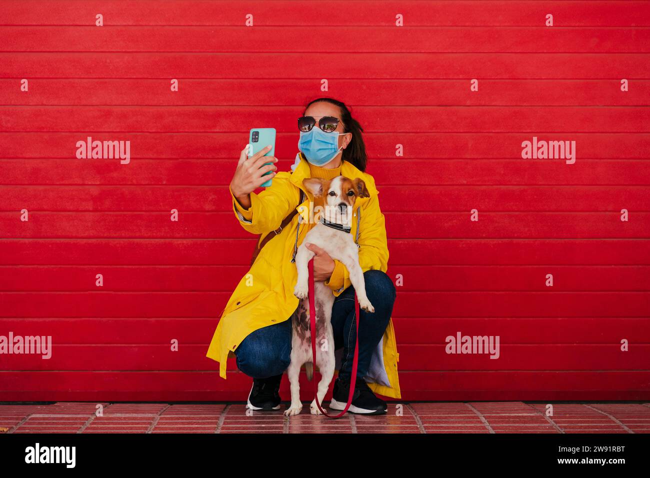 Donna che indossa la maschera facciale che fa selfie con il cane Foto Stock