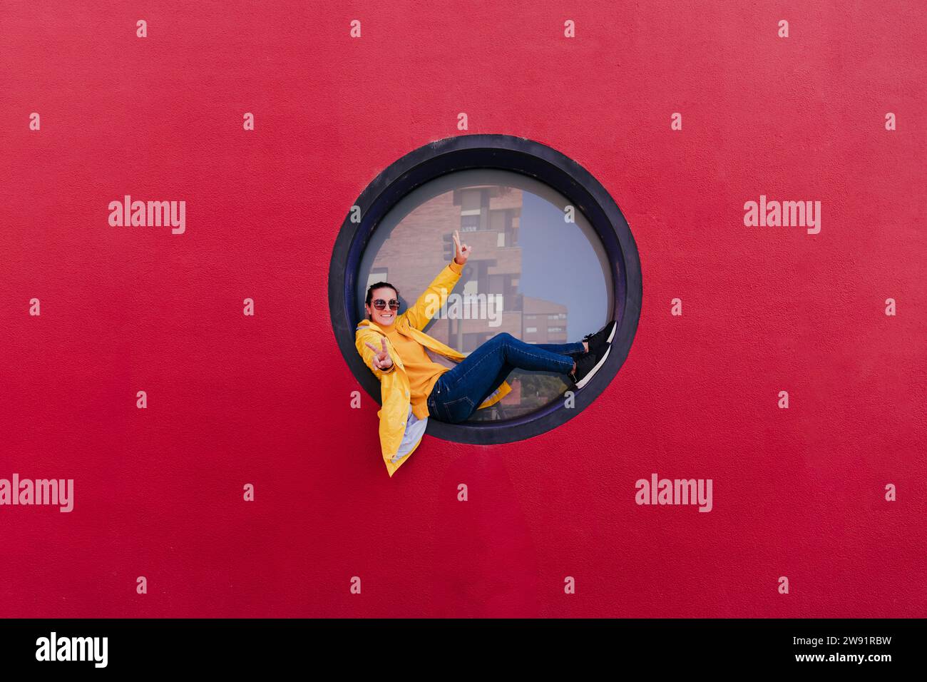 Donna con impermeabile giallo seduta nell'oblò che segna la vittoria Foto Stock