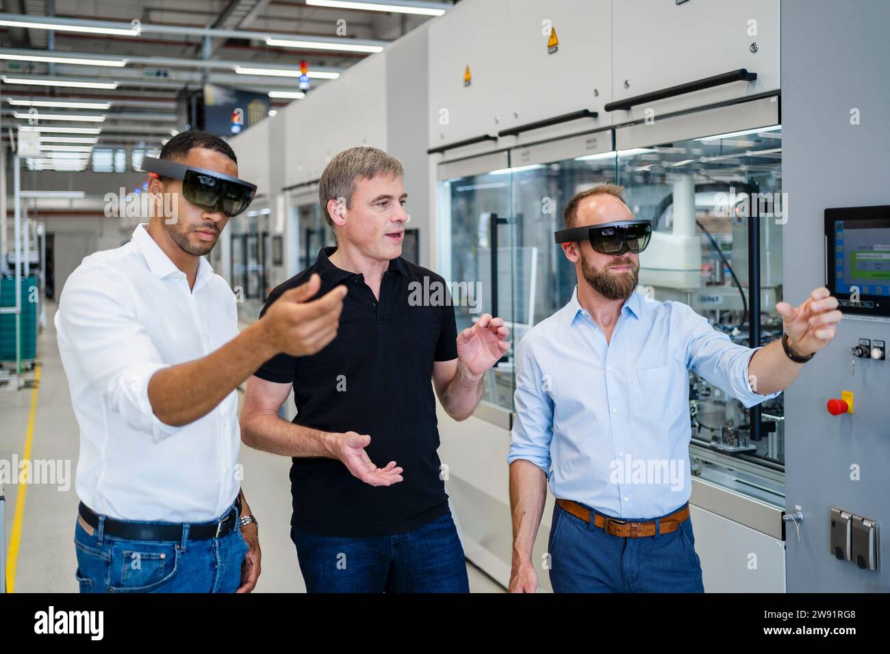 Due tecnici che indossano occhiali per realtà aumentata in fabbrica e interagiscono con i colleghi Foto Stock