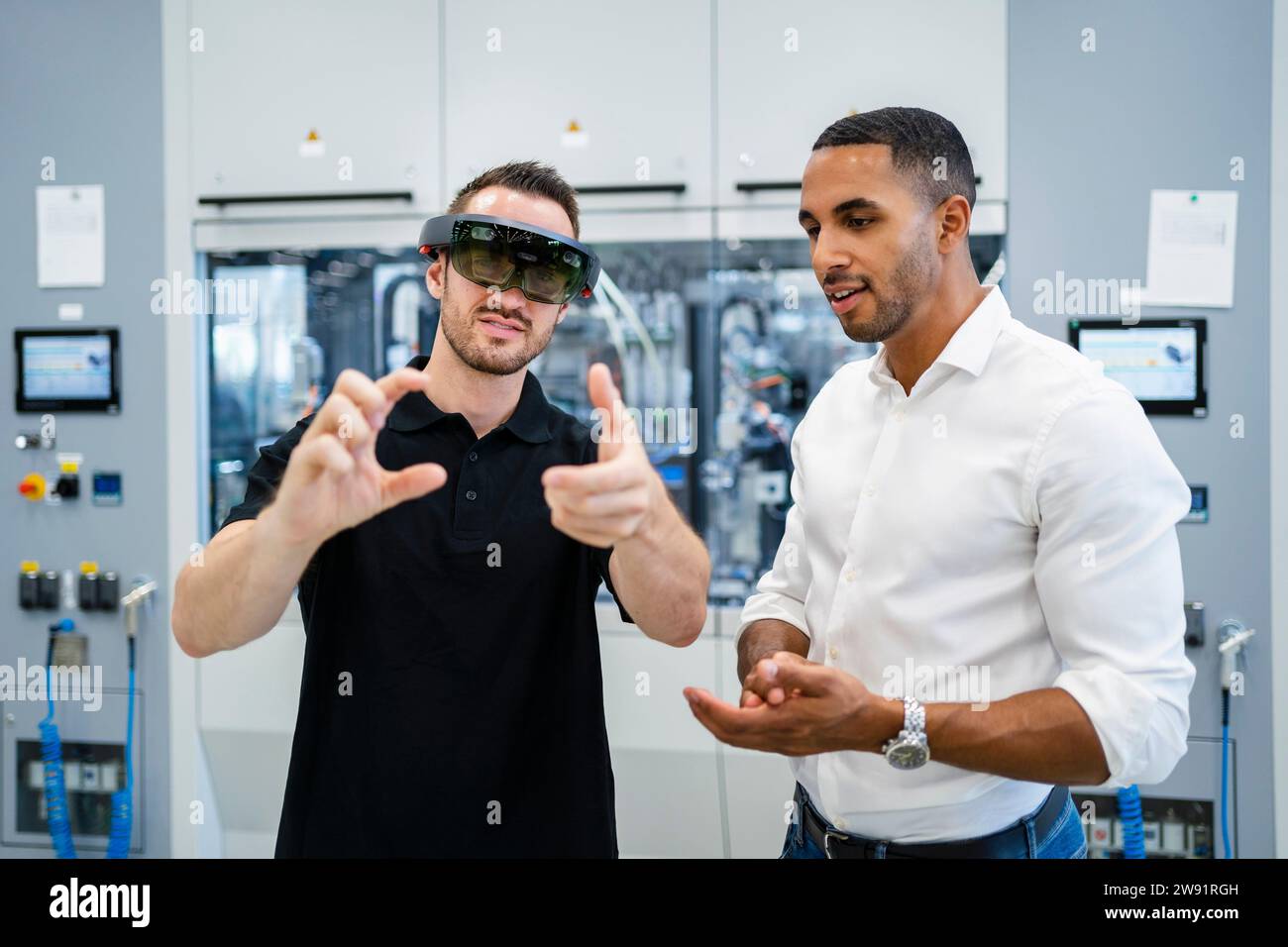 Tecnico che indossa occhiali per realtà aumentata in una fabbrica che interagisce con un collega Foto Stock
