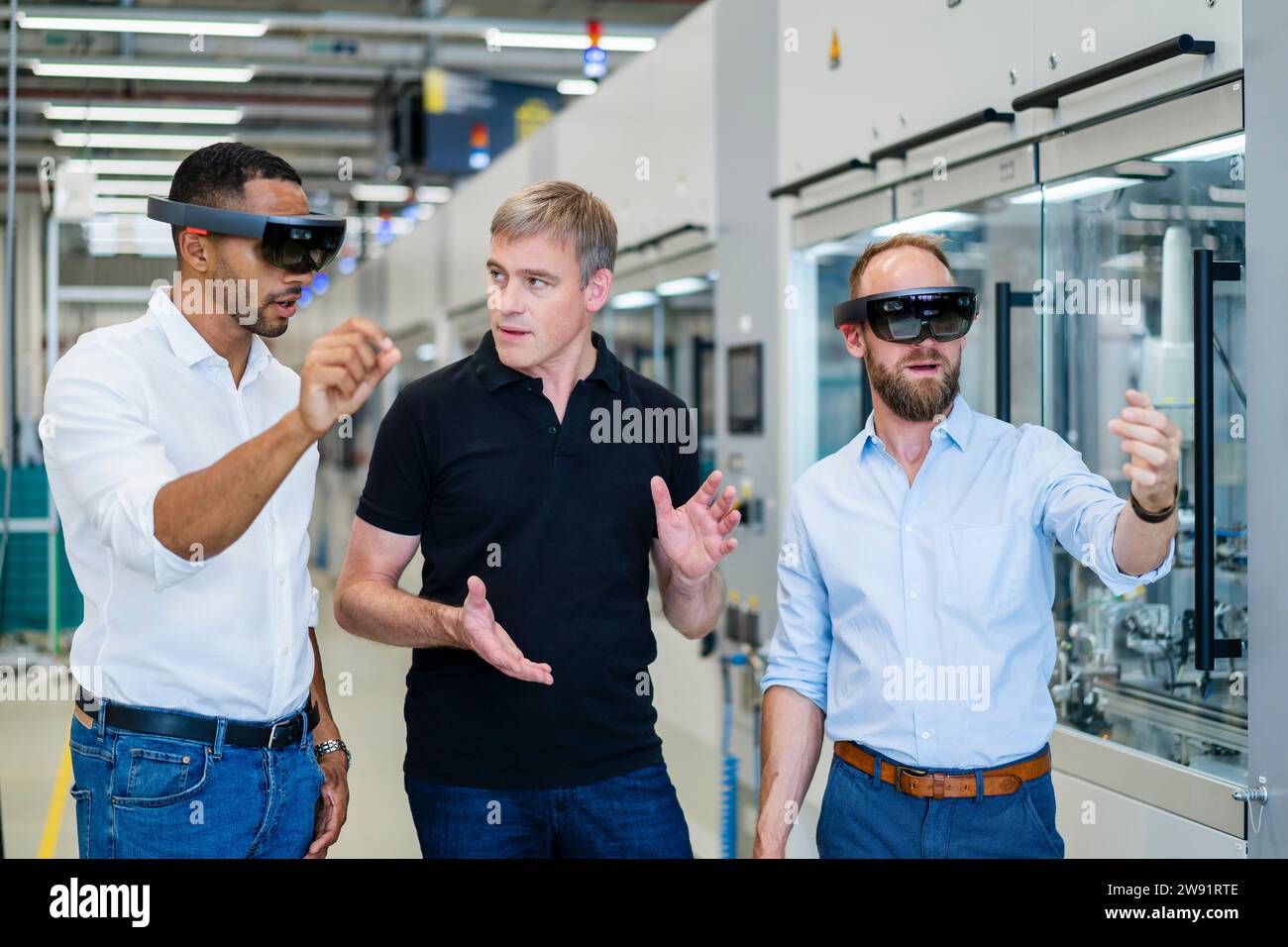 Due tecnici che indossano occhiali per realtà aumentata in fabbrica e interagiscono con i colleghi Foto Stock