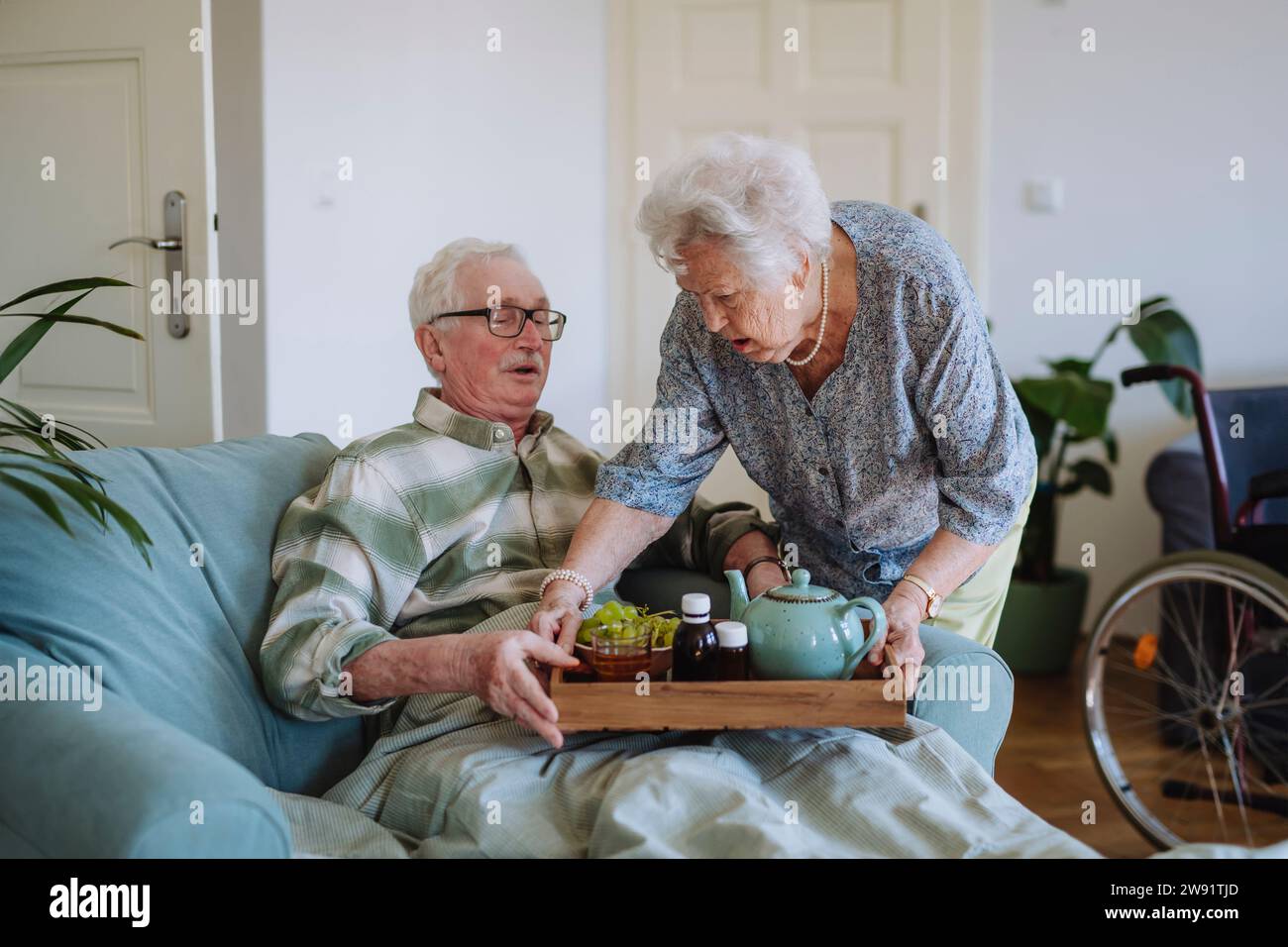 Donna anziana che serve cibo e bevande all'uomo seduto sul divano a casa Foto Stock