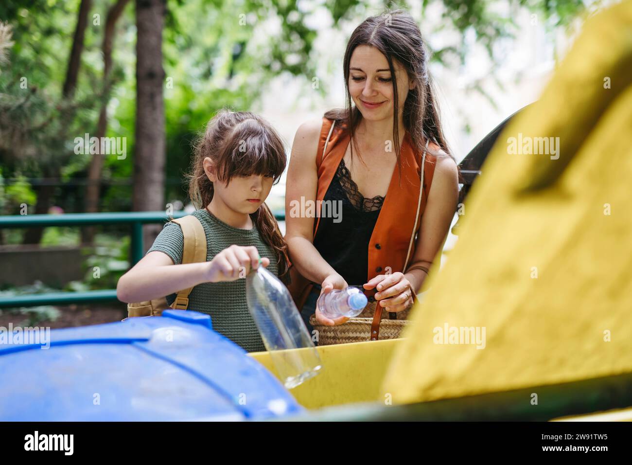 Madre e figlia studentessa separano i rifiuti in bidoni di riciclaggio in città Foto Stock