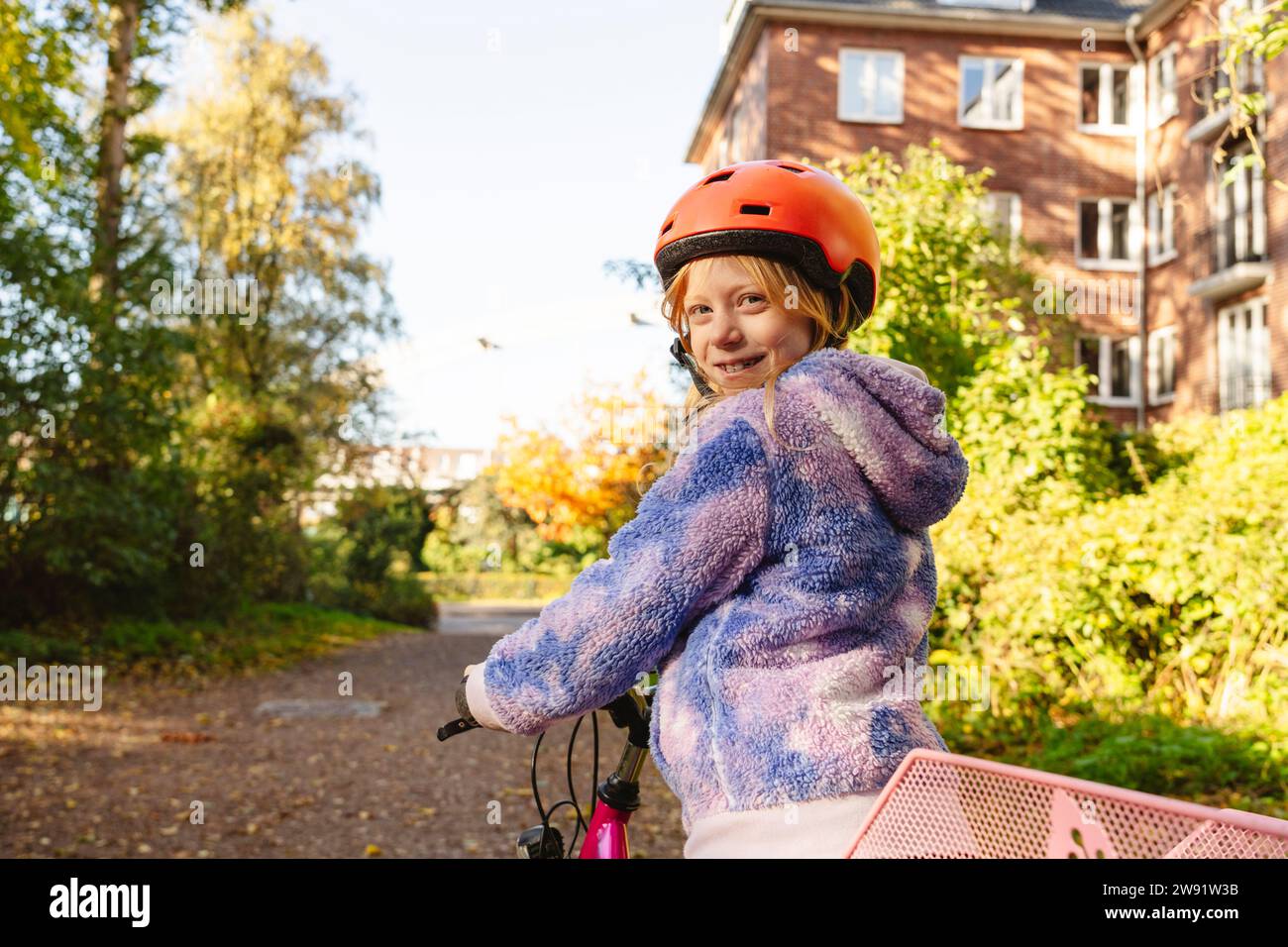 Ragazza sorridente che guarda a spalla con la bicicletta al parco Foto Stock