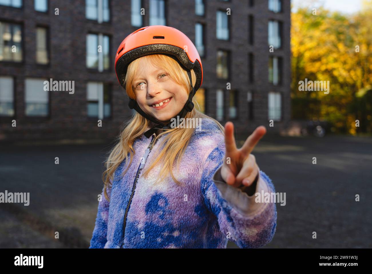 Ragazza sorridente che indossa il casco con gesti di pace con la mano Foto Stock