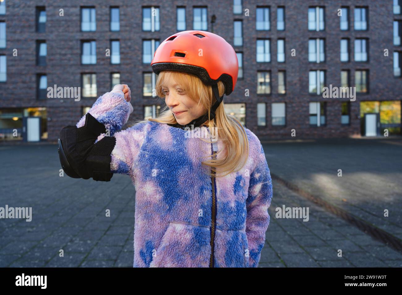 Ragazza sorridente che indossa indumenti protettivi e muscoli flessibili davanti all'edificio Foto Stock