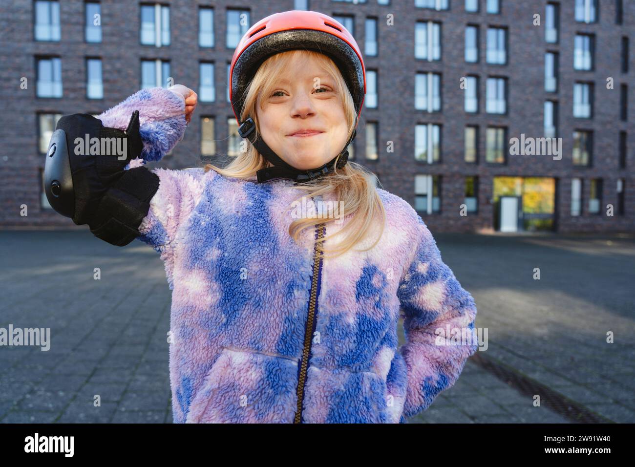 Ragazza sorridente con un dispositivo di protezione che flette muscoli davanti all'edificio Foto Stock