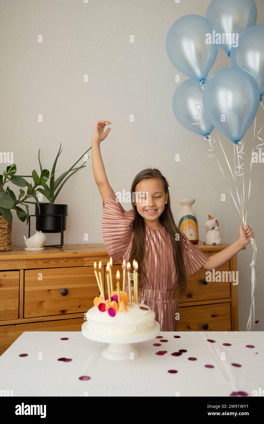 Ragazza allegra che tiene i palloncini e festeggia il compleanno con la torta a casa Foto Stock