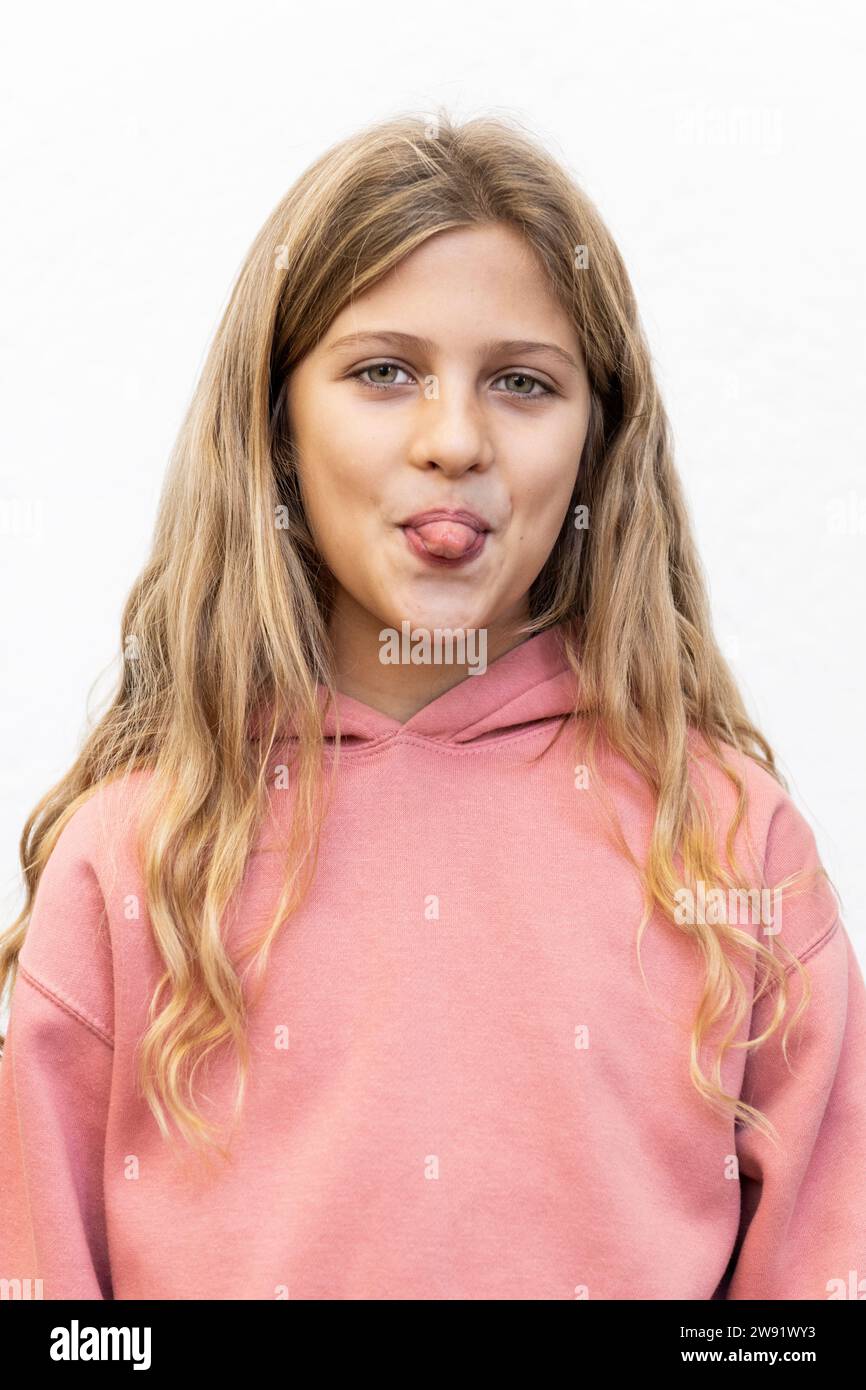 Giocosa ragazza bionda che sporge la lingua su sfondo bianco Foto Stock