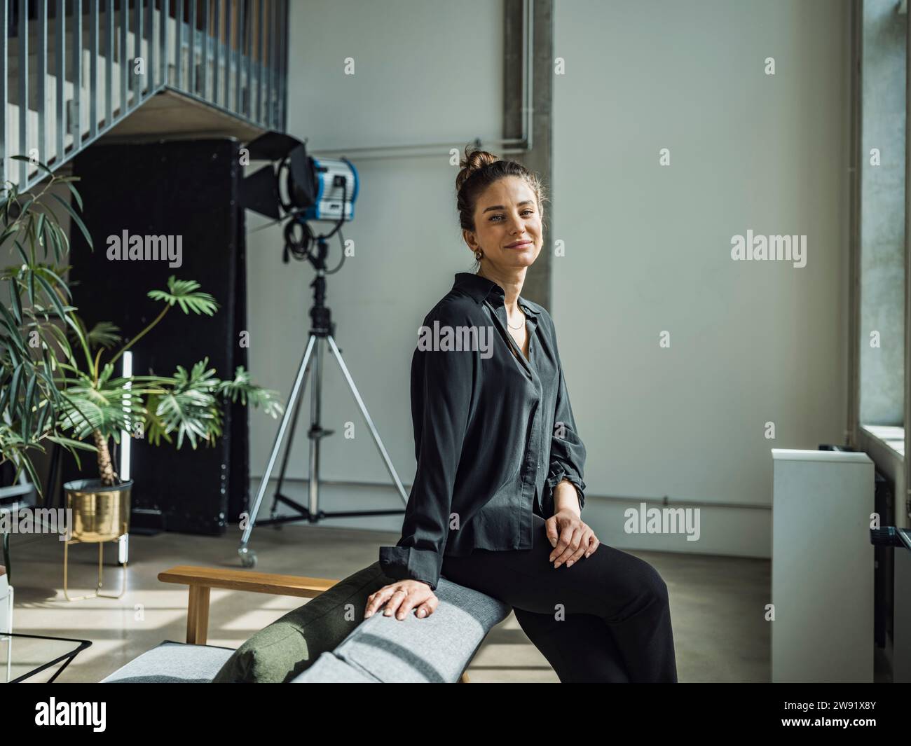Donna d'affari sorridente seduta con luce elettrica sullo sfondo a casa Foto Stock