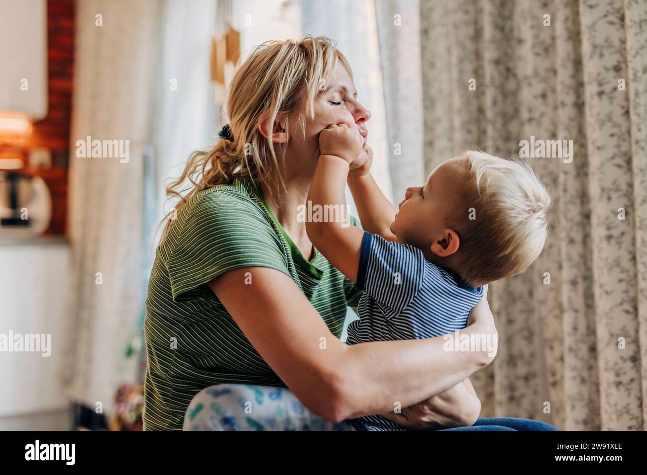 Figlio giocoso che tocca le mamme a casa Foto Stock