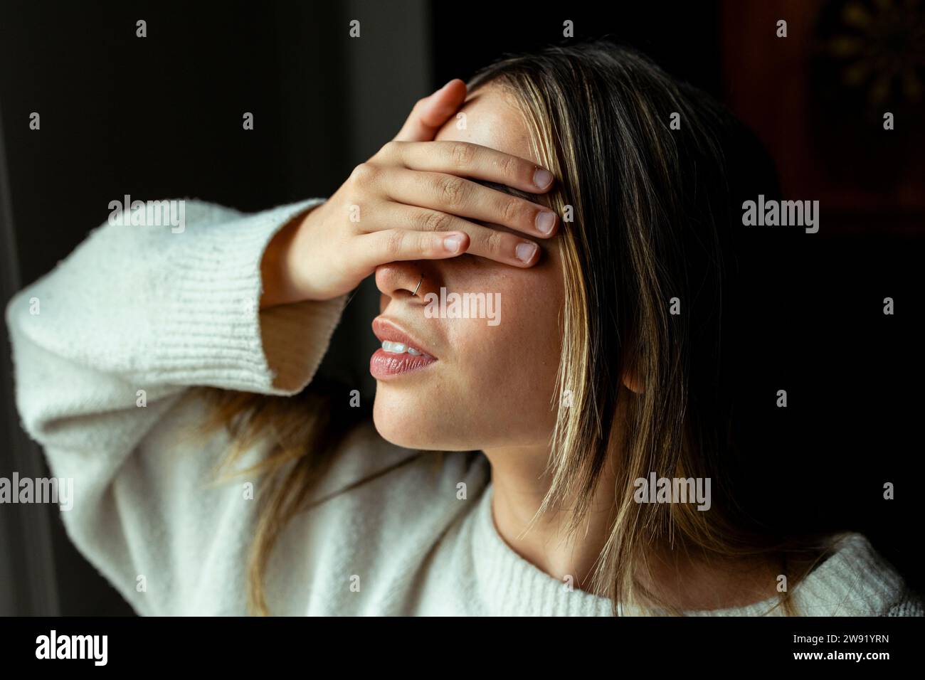 Giovane donna che copre gli occhi con la mano a casa Foto Stock