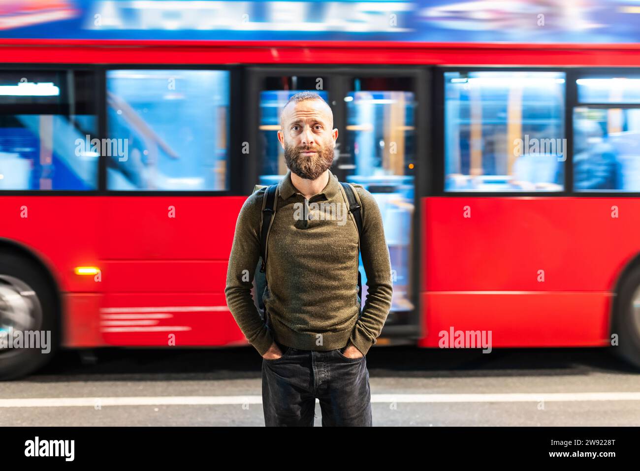 Uomo con le mani in tasca davanti a un autobus in movimento in città Foto Stock