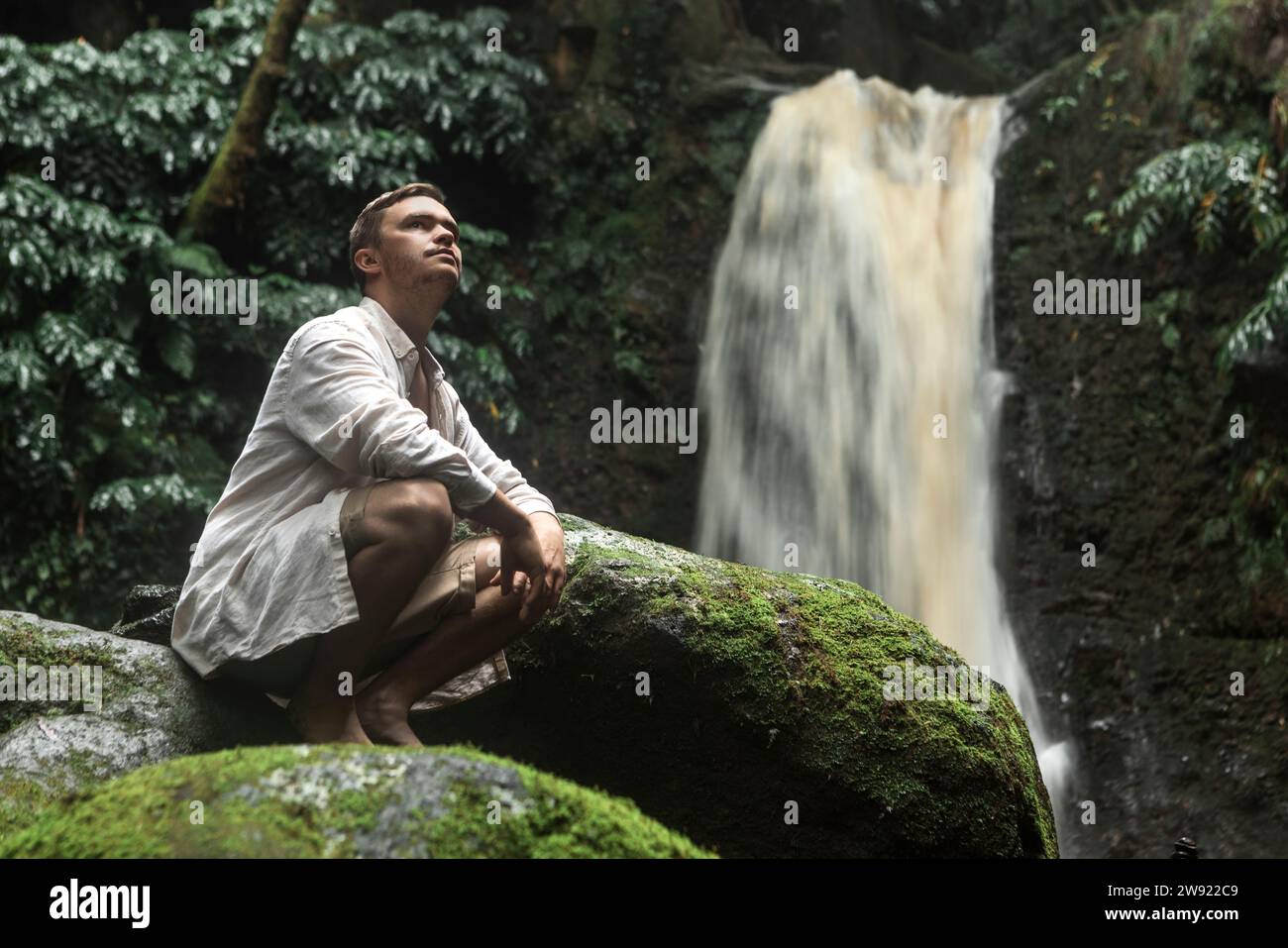 Un giovane premuroso accovacciato sulle rocce vicino alla cascata Foto Stock