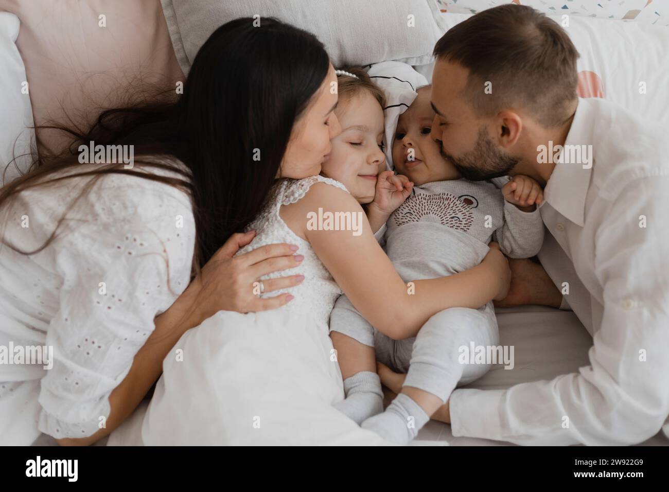 I genitori adorano baciare le guance dei bambini a letto a casa Foto Stock