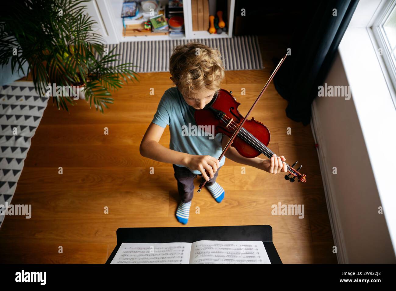 Ragazzo con i capelli biondi che pratica il violino davanti agli spartiti a casa Foto Stock