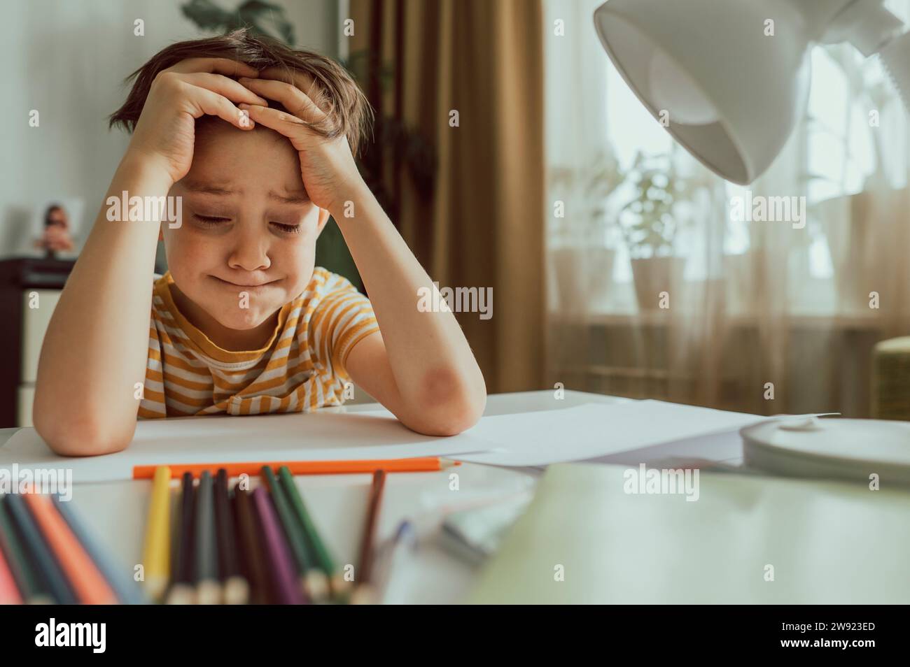 Ragazzo frustrato con gli occhi chiusi seduto alla scrivania Foto Stock