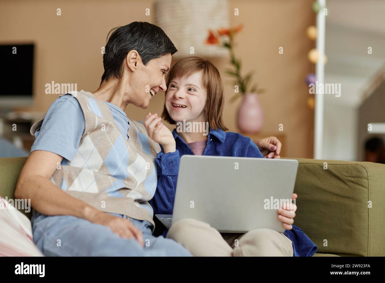 Madre felice e sua figlia con disabilità che tiene il portatile a casa Foto Stock