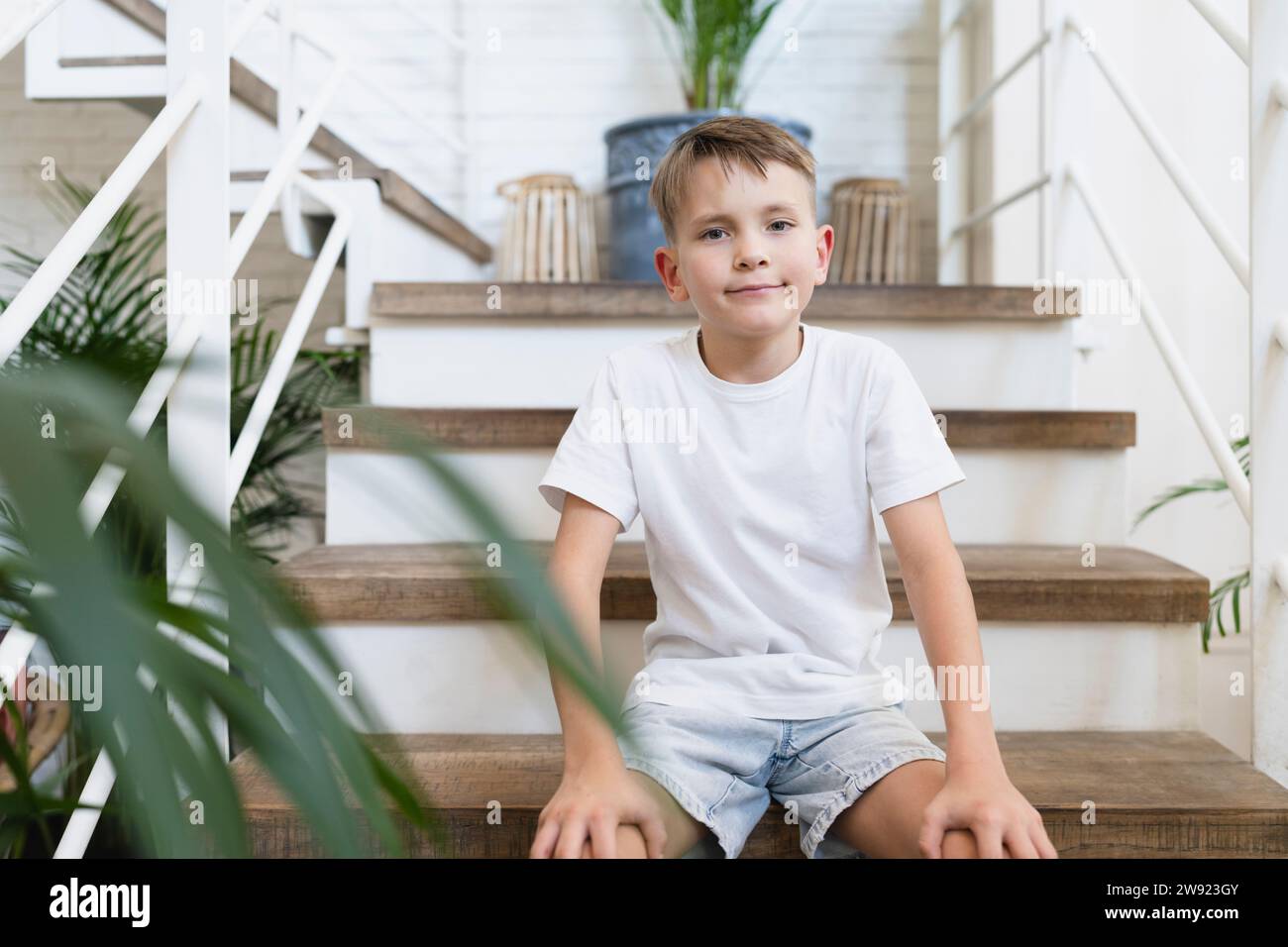 Biondo e carino ragazzo seduto sui gradini di casa Foto Stock