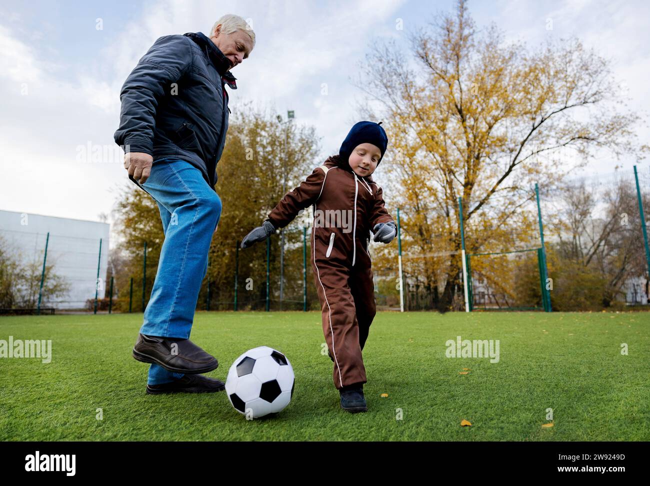 Uomo anziano e nipote che giocano con la palla al campo da calcio Foto Stock