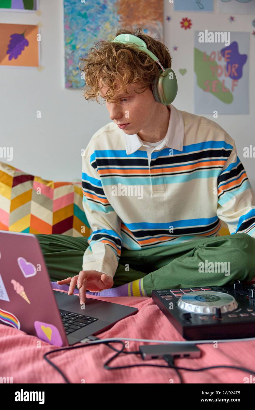 Uomo con cuffie che usa un computer portatile e che mixa la musica sulla scrivania a casa Foto Stock