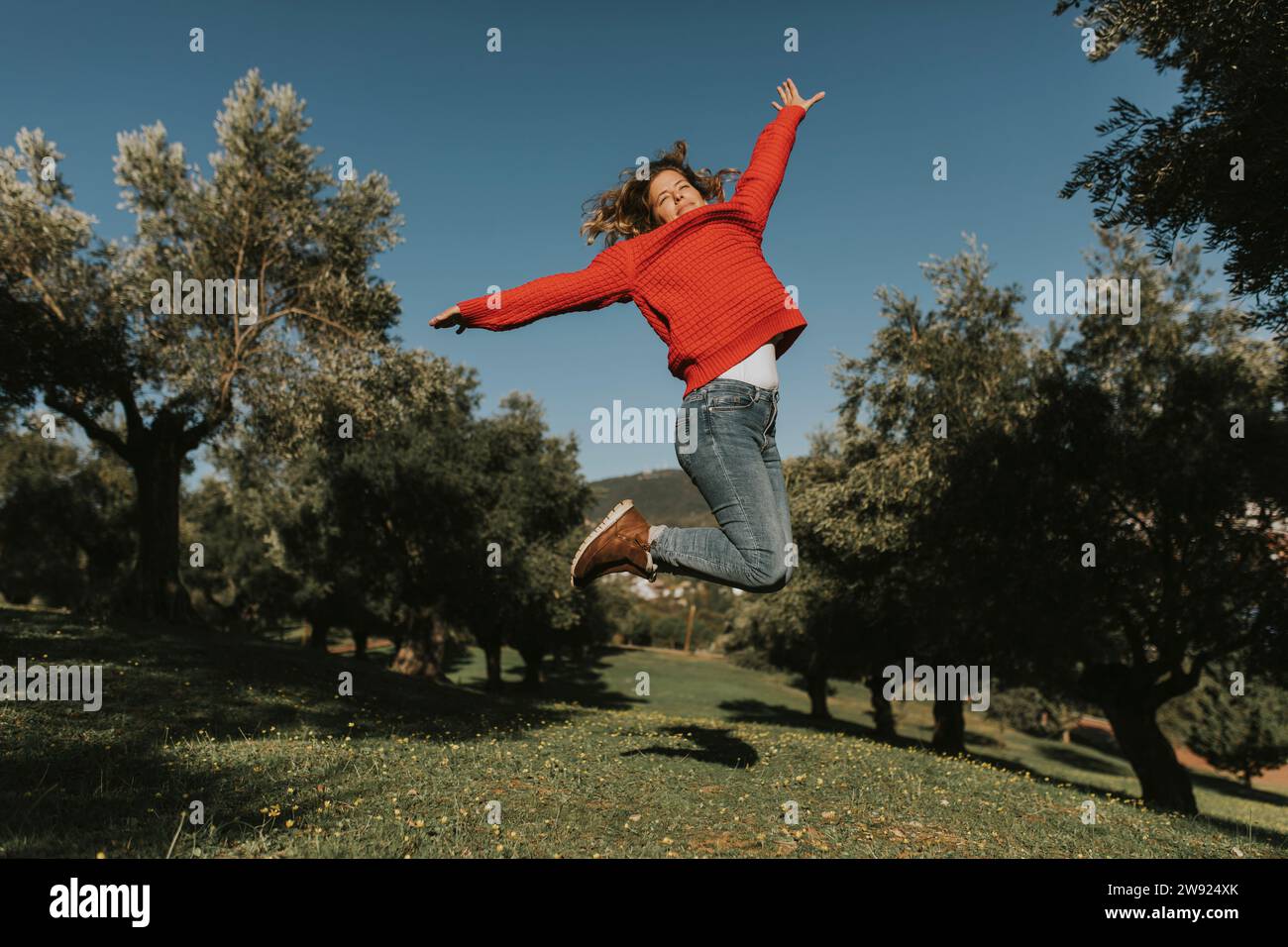 Donna felice che salta vicino agli ulivi nei campi nelle giornate di sole Foto Stock