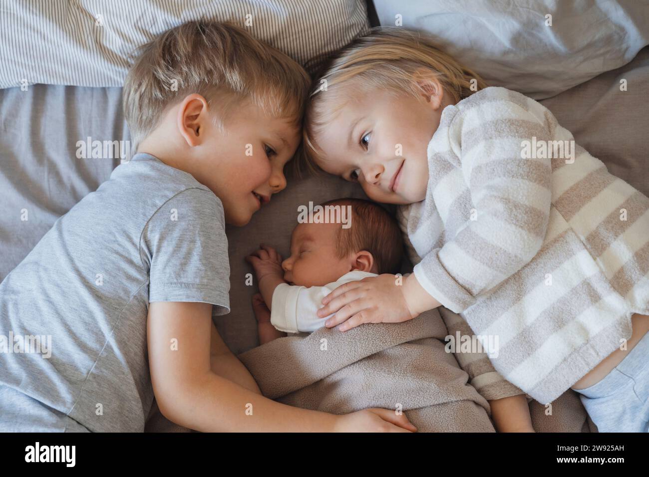 Neonato bambino che dorme vicino ai fratelli sdraiati a letto Foto Stock