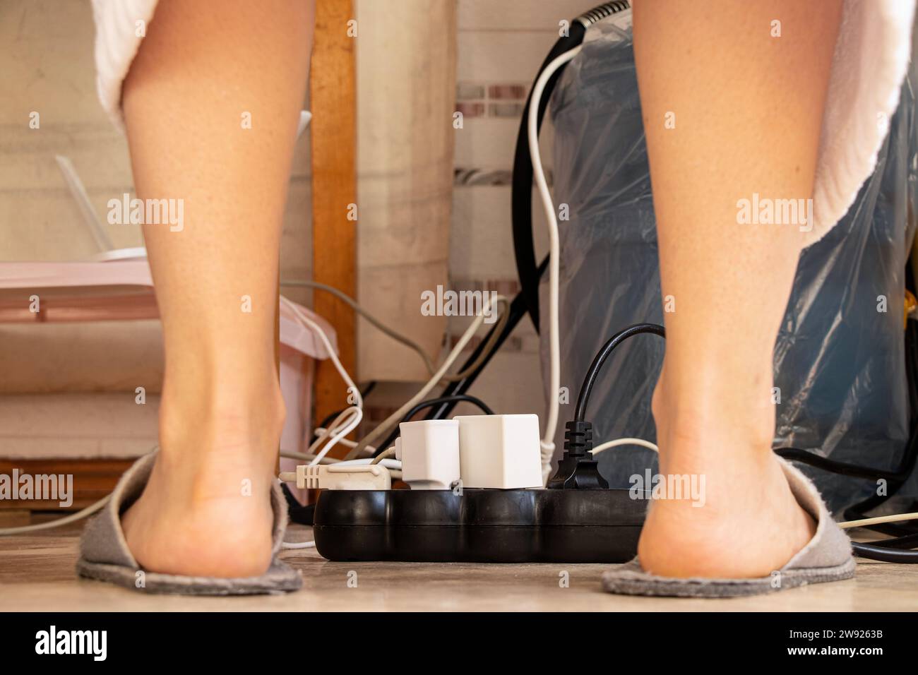 Un sistema di protezione da sovratensione si trova sul pavimento dell'appartamento e varie spine dei dispositivi elettronici sono bloccate e le gambe femminili nelle vicinanze, i fili e una carica Foto Stock