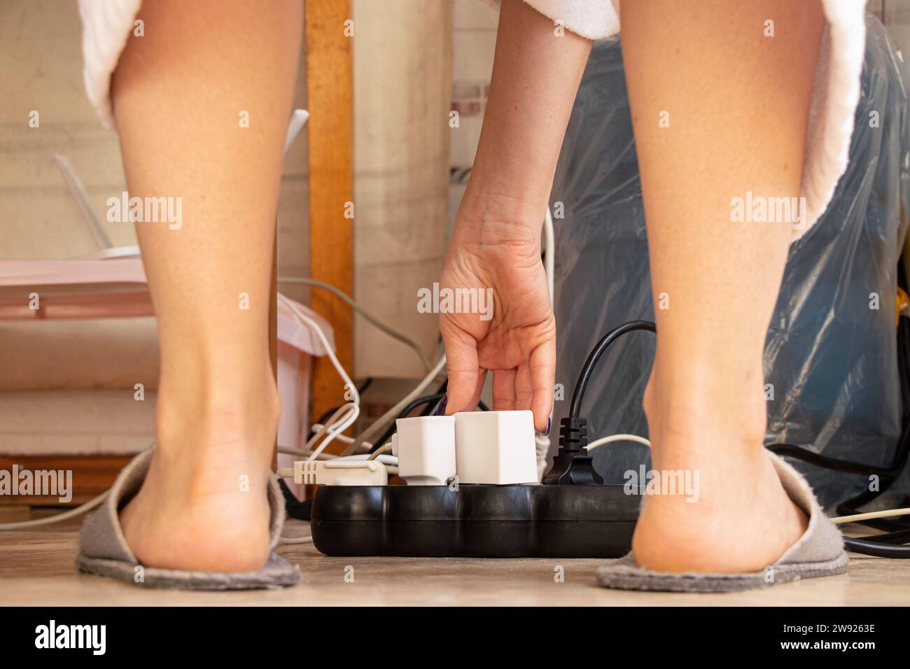 Un sistema di protezione da sovratensione si trova sul pavimento dell'appartamento e varie spine dei dispositivi elettronici sono bloccate e le gambe femminili nelle vicinanze, i fili e una carica Foto Stock