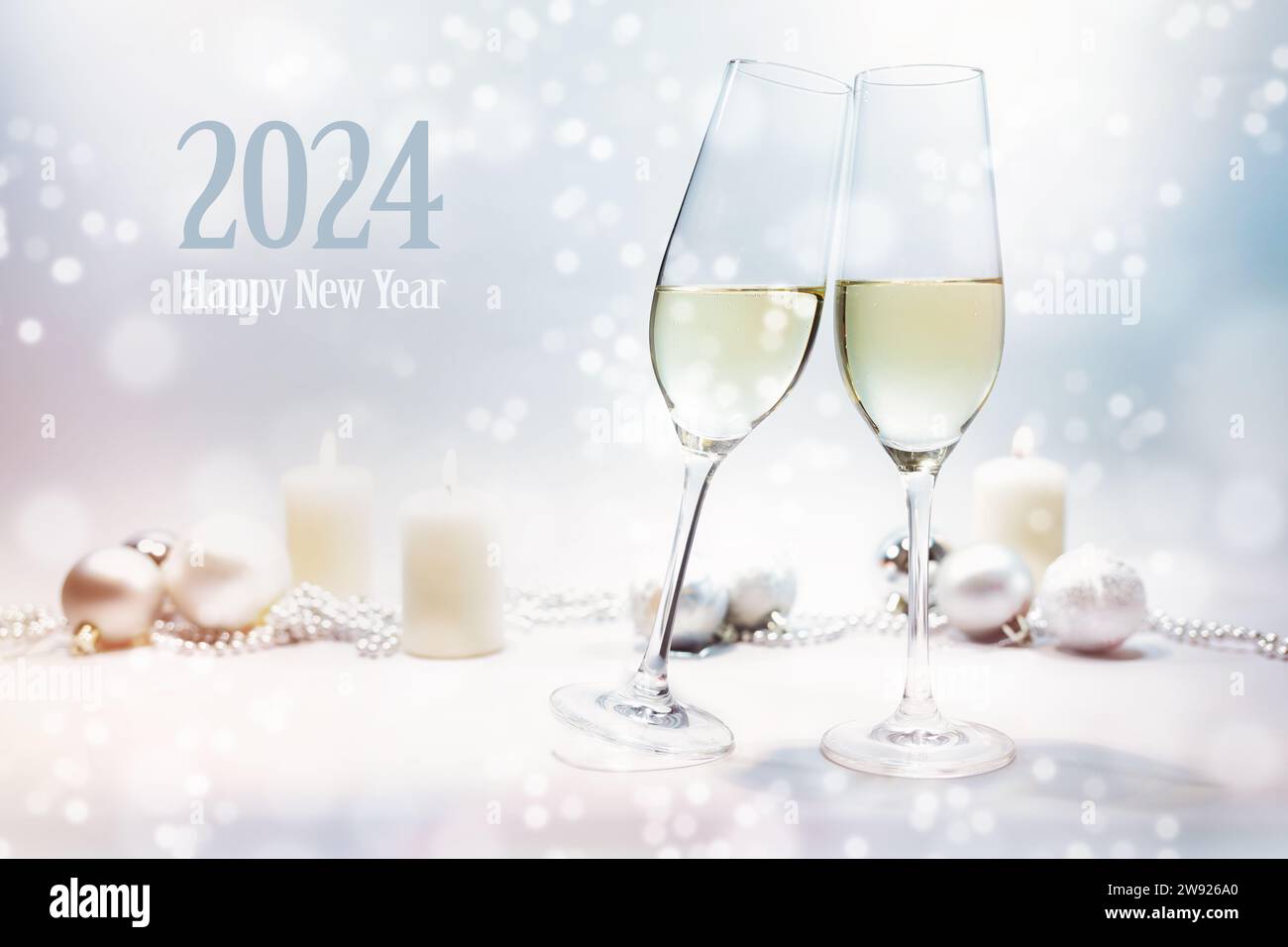 Testo felice anno nuovo 2024, brindisi con due bicchieri di champagne, sfondo luminoso con candele, bauble natalizi e bokeh innevato, messa a fuoco selezionata, profondità ridotta Foto Stock