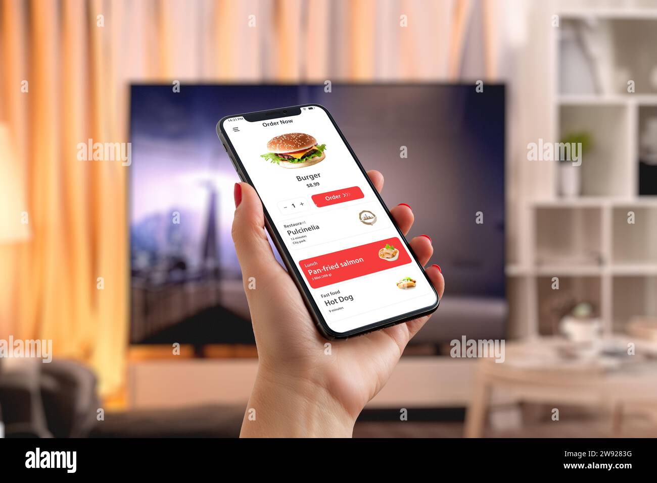 L'uomo ordina un hamburger tramite smartphone nel soggiorno, creando un mix perfetto di praticità tecnologica e piacere nel fast food davanti al televisore Foto Stock