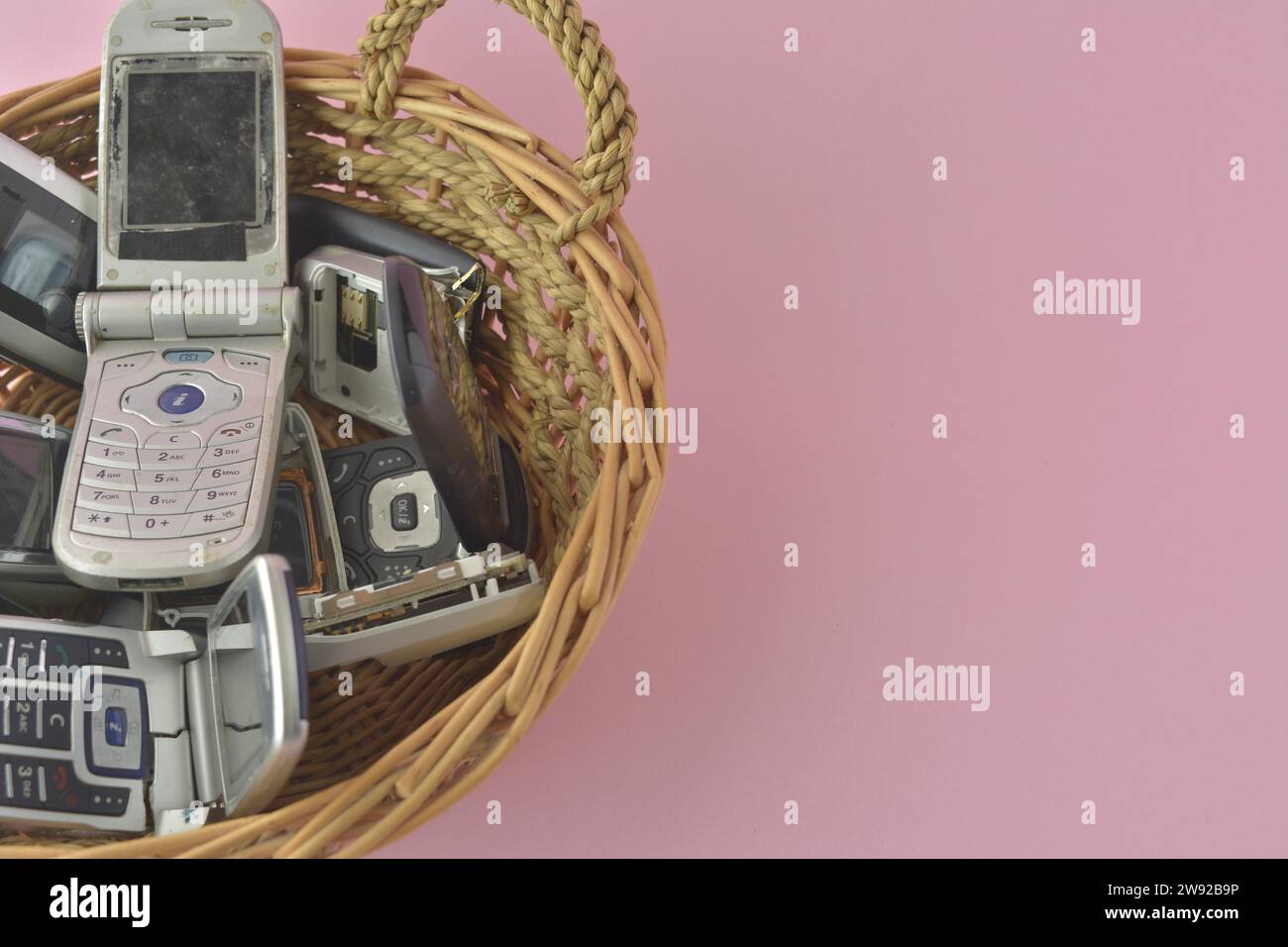 Vecchi telefoni cellulari che fuoriescono da un cestino, adagiati su uno sfondo rosa, carte da poker e patatine Foto Stock