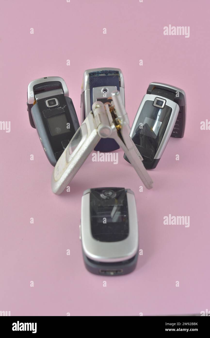 Una collezione di vecchi telefoni cellulari con un telefono ribaltabile davanti su sfondo rosa, carte da poker e patatine Foto Stock