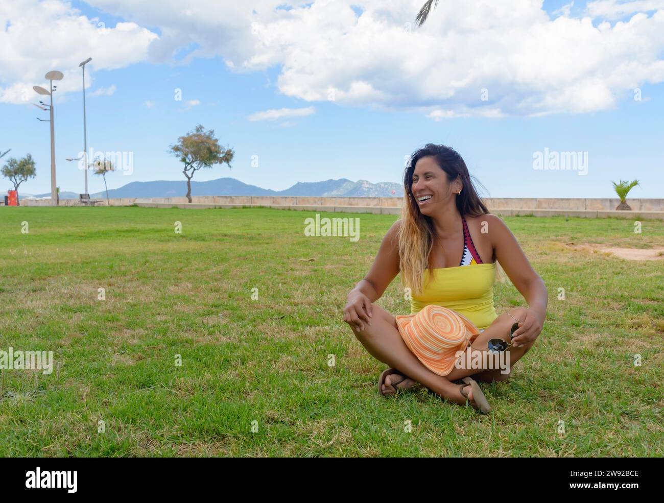 Bella donna latina di 40 anni, sorridente seduta sull'erba di un parco di Maiorca, isole baleari, concetto di vacanza Foto Stock