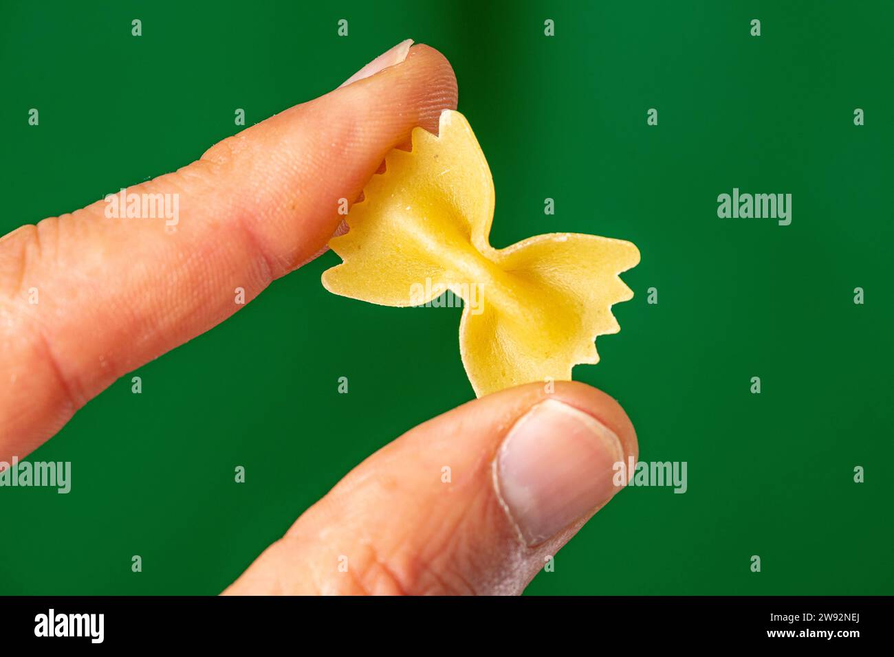 pasta a forma di ansa di grano tra le dita sotto lo sfondo verde Foto Stock
