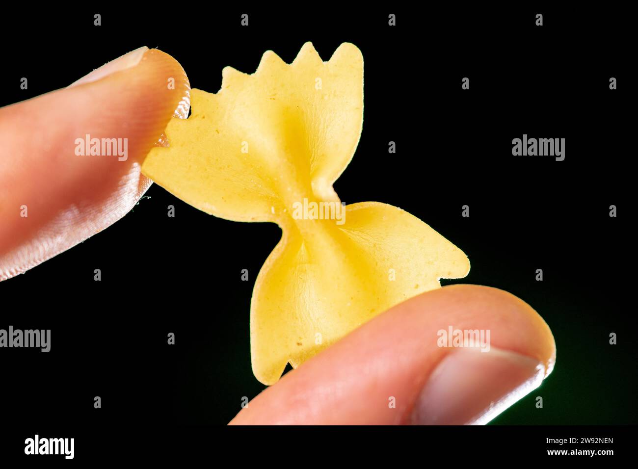 pasta a forma di ansa di grano tra le dita sotto lo sfondo verde Foto Stock