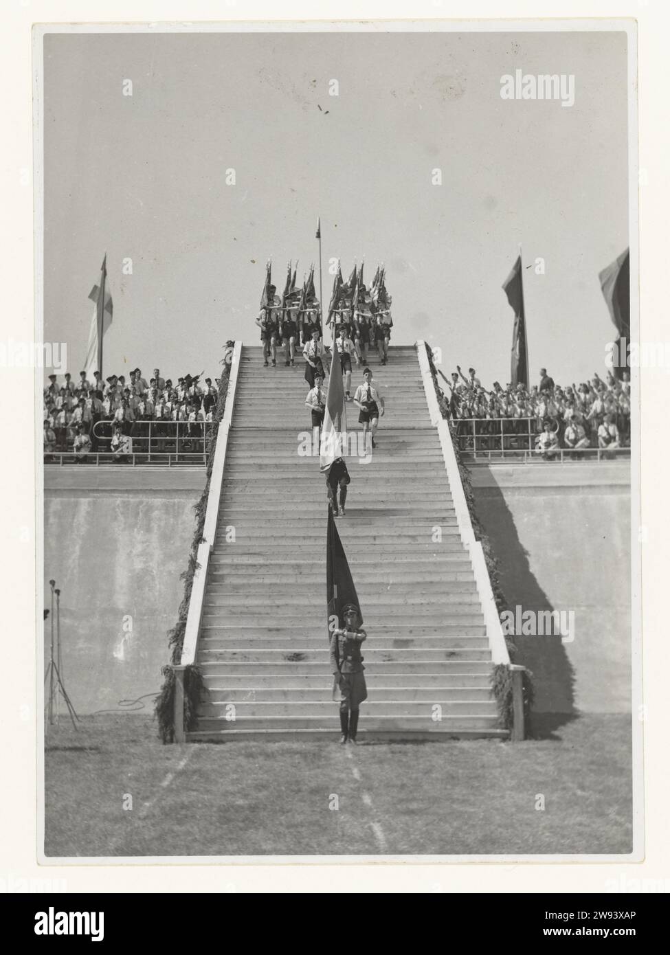 Tempesta giovanile allo stadio Galgenwaard, 1942 fotografa Una lunga fila di membri della Jeugdstorm che scende dallo stadio allo stadio Galgenwaard di Utrecht il 20 giugno 1942. Nello stadio assisteranno ai giurati di 3000 dirigenti della NSB, in fondo alle scale c'è un soldato della Wehrmacht con una bandiera. Ci sono membri della tempesta giovanile nelle tribune, a sinistra e a destra delle scale. Una parte porta il saluto dell'NSB: Braccio allungato come il saluto di Hitler e chiama: Houzee. La cerimonia del giuramento fu il risultato di un compromesso tra i tedeschi e l'NSB, i tedeschi non volevano un giuramento Foto Stock