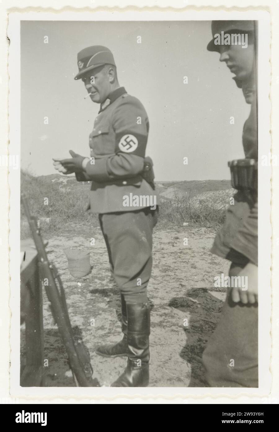 Membro del Reichsarbeitsdienst, 1940 - 1942 Fotografia Un membro del Reichsarbeitsdienst con una svastica intorno al braccio si trova da qualche parte nelle dune. Alla sua sinistra alcune pistole, alla sua destra di un soldato della Wehrmacht. Sul retro: Abteilungsführer Oberstfeldmstr. Ewers Paesi Bassi supporto fotografico gelatina stampa argento occupazione  guerra Paesi Bassi Foto Stock