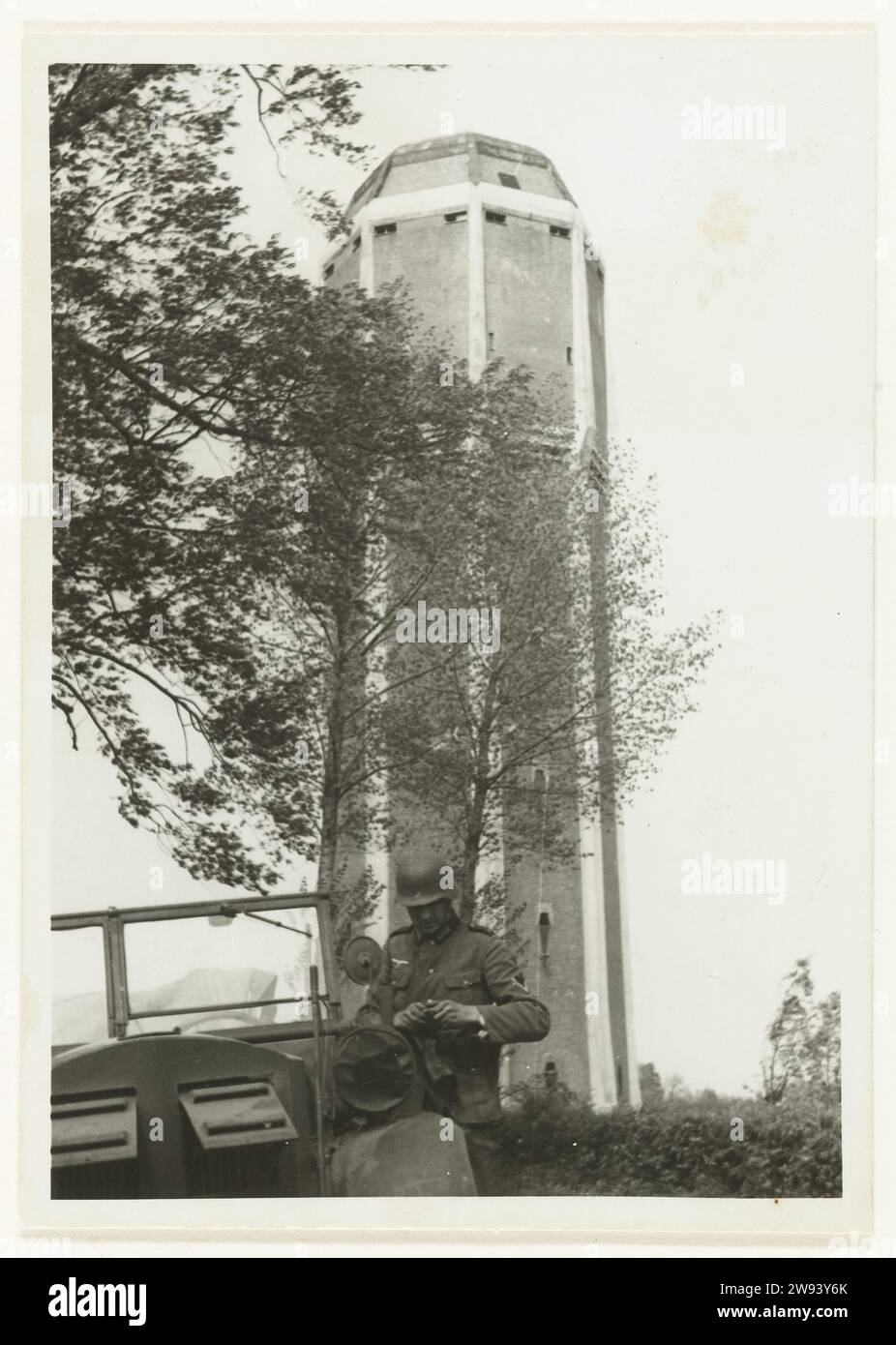 Wehrmacht Militair at a Water Tower, 1940 Fotografia Un militare della Wehrmacht è in macchina, dietro di lui c'è una torre dell'acqua. Questo deve servire da punto di osservazione. Sul retro c'è scritto: AUF D. Wasserturm von Dongen. Supporto fotografico Dong stampa argento gelatina occupazione  guerra. Torre dell'acqua Dong Foto Stock