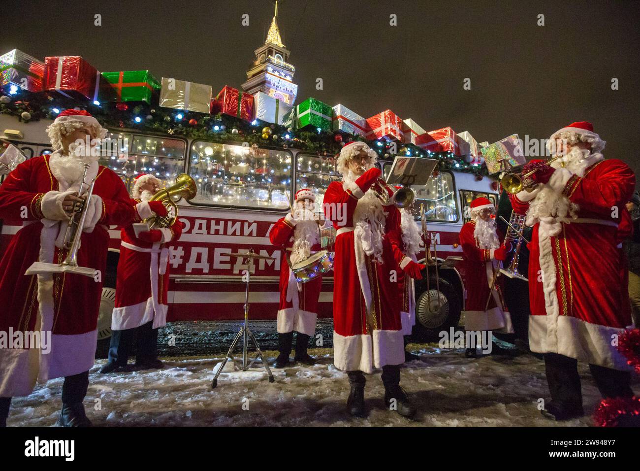 Pechino, Russia. 23 dicembre 2023. Le persone vestite da padre Frost suonano strumenti musicali di fronte a un autobus con decorazioni festive a St Pietroburgo, Russia, 23 dicembre 2023. Crediti: Irina Motina/Xinhua/Alamy Live News Foto Stock