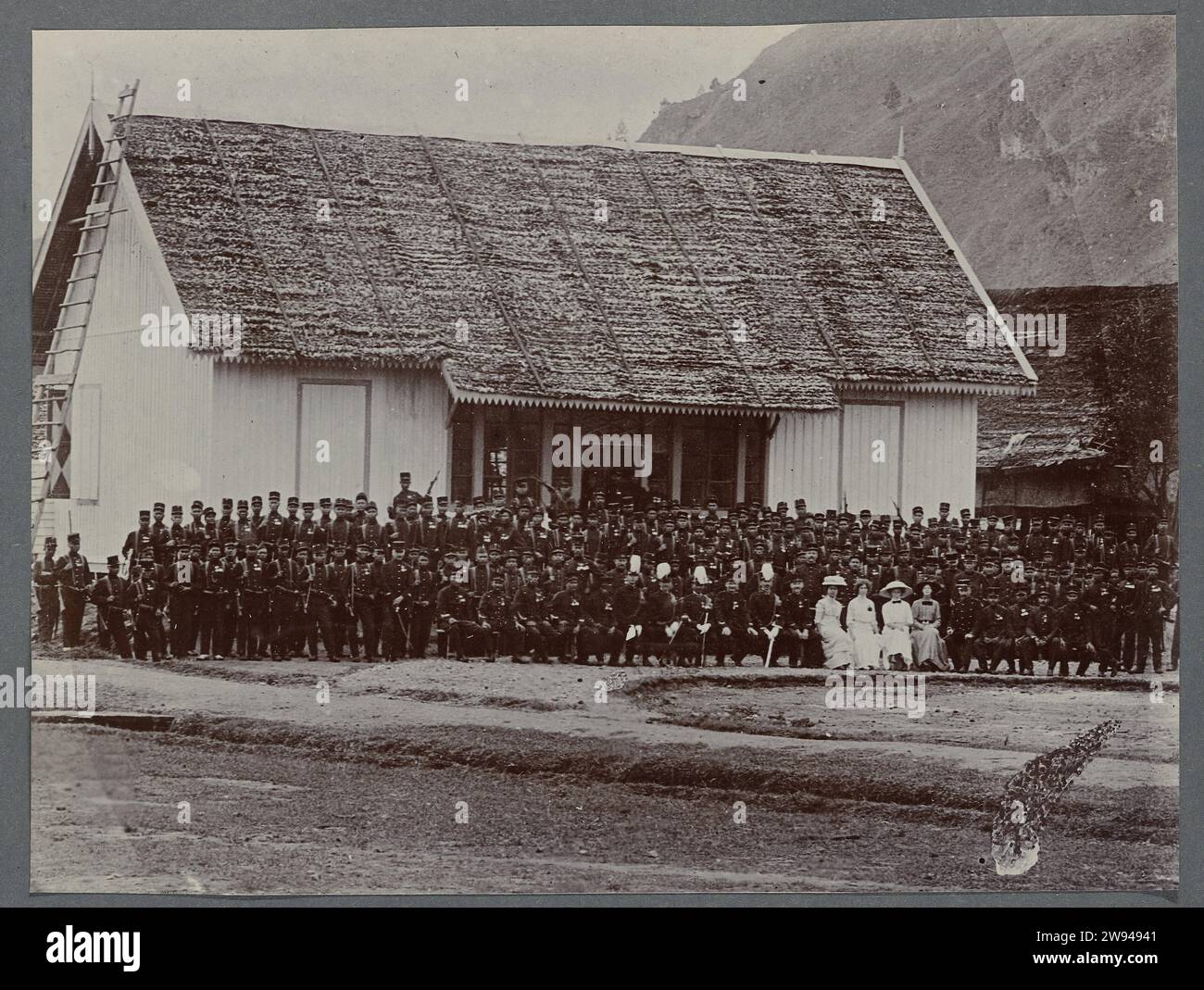 Foto di gruppo di soldati, foto 1903 - 1913 che posa un grande gruppo di soldati del KNIL di fronte a una casa. Al centro della prima fila alcuni ufficiali superiori con piume bianche sull'elmetto e quattro donne. Lo stesso gruppo delle foto della cerimonia giurata. Foto imballata in un album con 87 foto sulla costruzione del Gajoweg a Noord-Sumatra tra Bireuen e Takinguen tra il 1903 e il 1914. Supporto fotografico Noord-sumatra Gajoweg Foto Stock