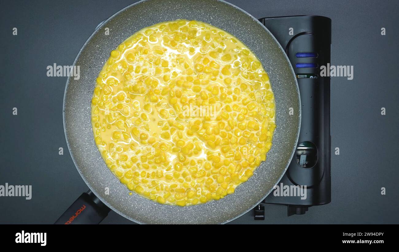 Cucinare una deliziosa colazione a base di mais su una stufa a gas portatile in una padella Foto Stock