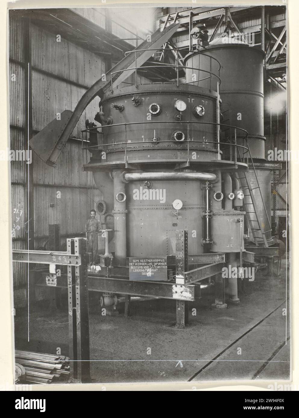Semi kestner, 1930 Fotografia semi Kestner realizzata nel 1930 e destinata alla fabbrica di zucchero Pesantren a Kediri. A sinistra della macchina si trova un operaio in fabbrica. Parte di un gruppo di foto più grandi e sciolte di diversi tipi di macchine dal N.V. Machinefabriek Braat a Surabaya, del periodo ca. 1920-1940. Supporto fotografico Surabaya stampa argento gelatina Java Foto Stock