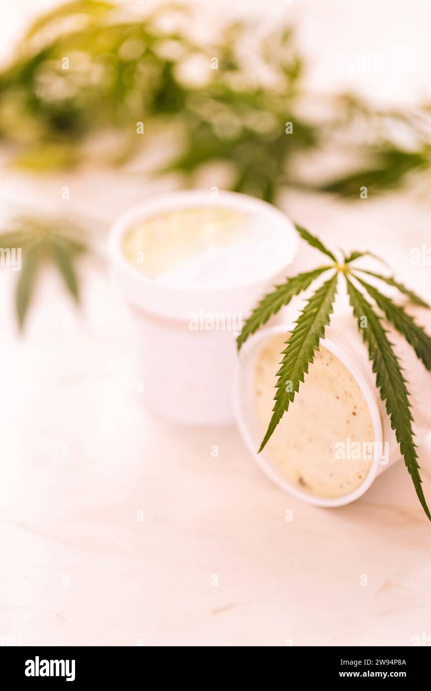 Una foglia di canapa è adagiata su un bicchiere di gelato su un tavolo di marmo bianco. Foglie di cannabis verde sullo sfondo. Cibo biologico e salute. Foto Stock